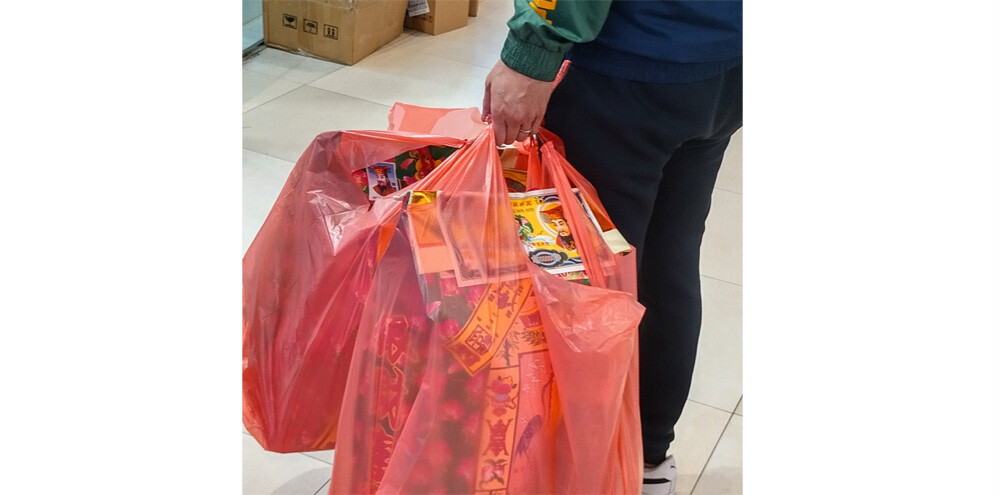A man carrying bags of joss paper goods in a shopping mall, Tai Po, HK