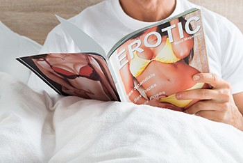 6 Baffling Robert Pattinson Stories That Raise More Questions Than Answers - a man reading a magazine titled EROTIC in bed