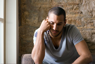 Photograph of a man in a grey shirt next to a window looking pensively