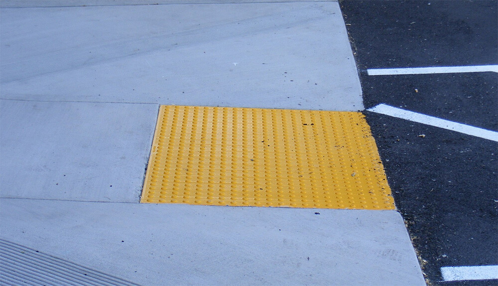 A set of yellow truncated domes can be seen on the down-ramp in a parking lot.