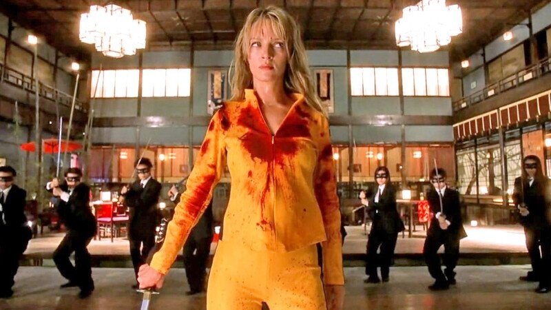 Woman in yellow tracksuit holding a knife facing men in black suits holding swords in traditional Japanese room